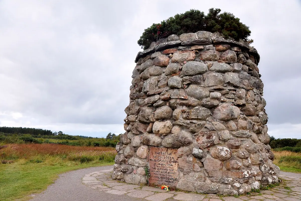 The stone memorial cairn on Culloden Battlefield, with moorland behind under a cloudy sky